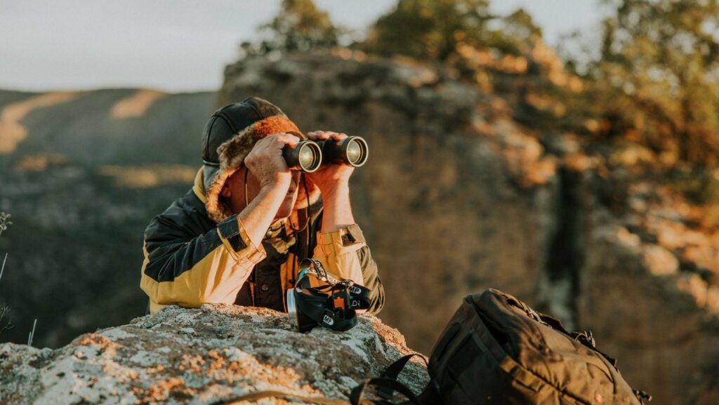 an adventurer observes through binoculars in a canyon at dusk